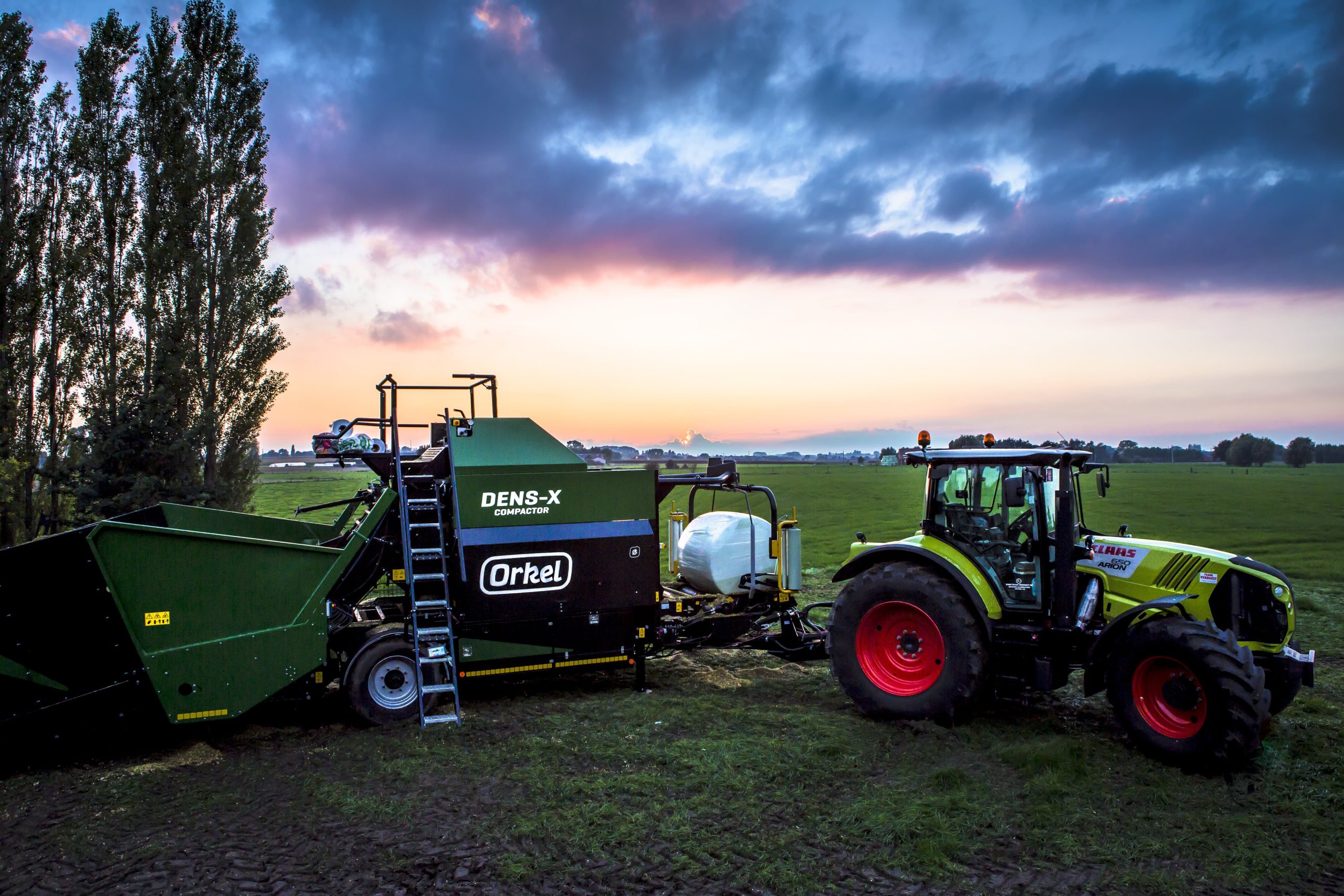 A Dens-X compactor and a tractor, with green grass and pink skies and heavy clouds.