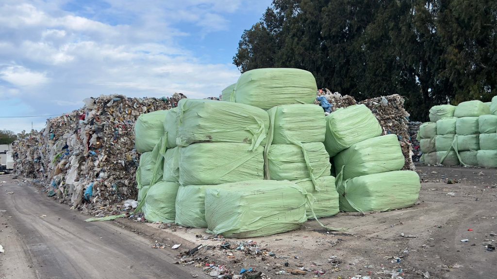 Stacks of tightly packed square bales of waste materials in a waste processing plant. The bales, made of compressed recyclables or discarded materials.