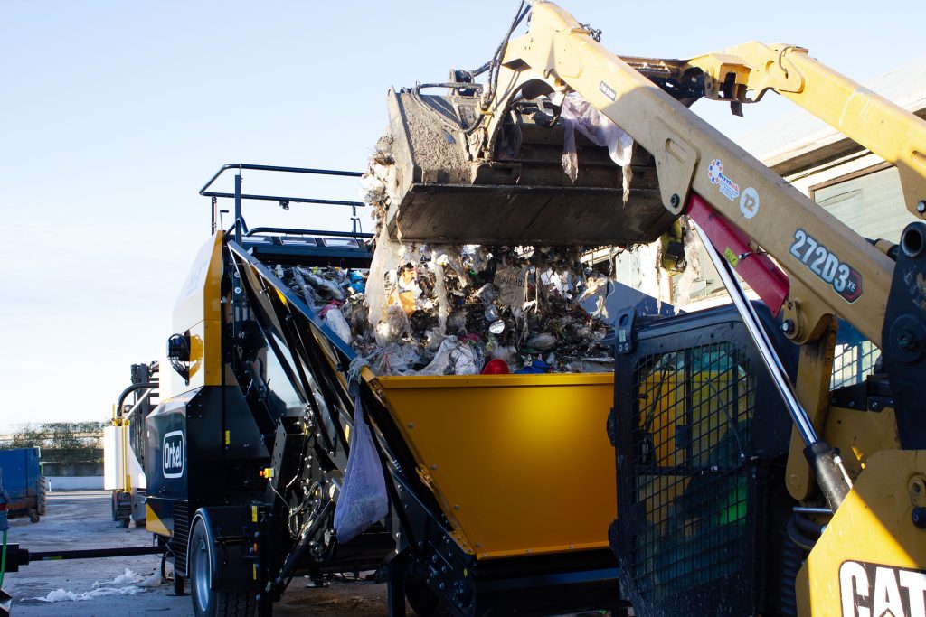A front loader emptying waste into the feed hopper of an Orkel compactor.