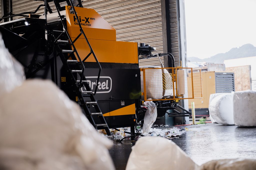A yellow industrial machine in a big waste management building. Plastic waste visible in the foreground.
