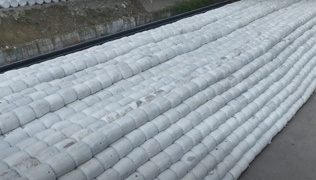 A big stack of round bales stacked neatly on a concrete ground outside, seen from above