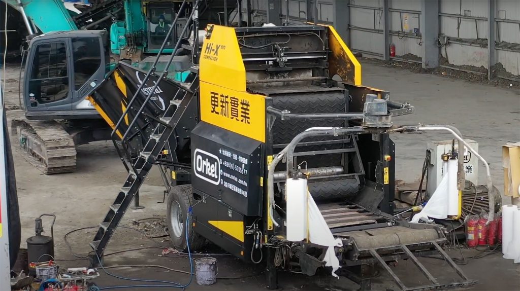 Overview of an yellow industrial baler standing in a big shed with concrete flooring